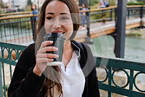 Smiling young woman drinks coffee outside