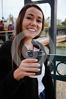 Smiling young woman drinks coffee outside