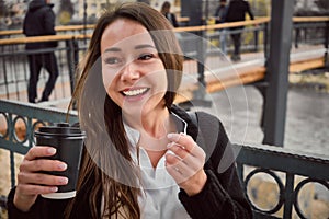 Smiling young woman drinks coffee outside