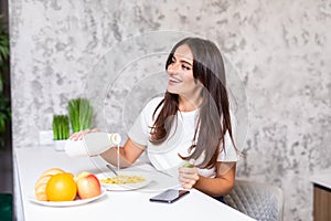 Smiling young woman eating breakfast cereals of bowl at home