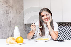 Smiling young woman eating breakfast cereals of bowl at home