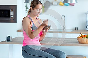 Smiling young woman eating cereals with strawberries while sitting in the kitchen at home