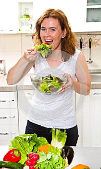 Smiling young woman eating fresh salad in modern kitchen