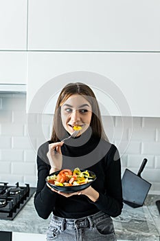 Smiling young woman eating fresh salad in modern kitchen