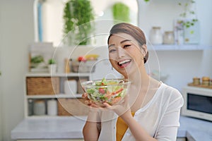 Smiling young woman eating fresh salad in modern kitchen