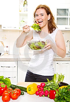 A Smiling young woman eating fresh salad in modern kitchen