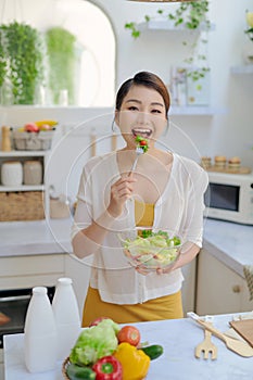 Smiling young woman eating fresh salad in modern kitchen