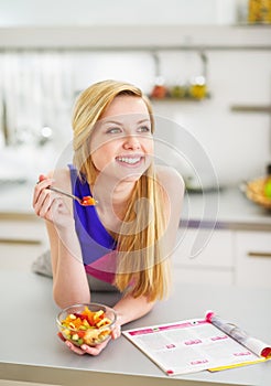 Smiling young woman eating fruits salad in kitchen