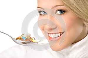 Smiling young woman eating a lot of pills on spoon