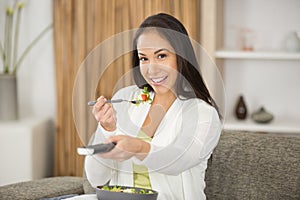 smiling young woman eating salad and watching tv at home