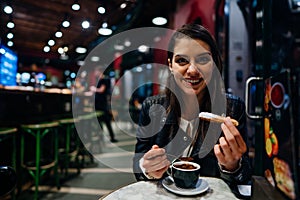 Smiling young woman eating traditional spanish churros with sugar dipped in hot chocolate sauce  in a original spanish style cafe.