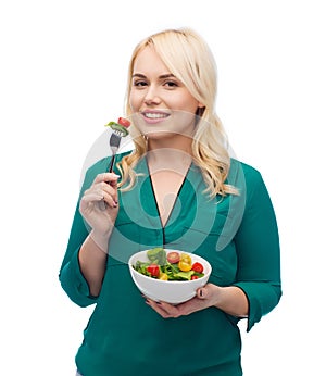 Smiling young woman eating vegetable salad