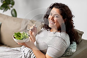 Smiling young woman eating vegetable salad at home