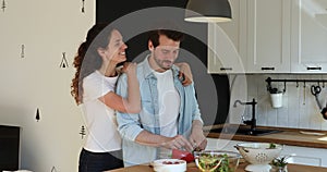 Smiling young woman embracing handsome husband preparing food.