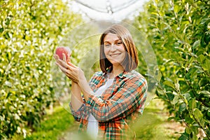 A smiling young woman farmer carefully holds a ripe red apple with both hands.