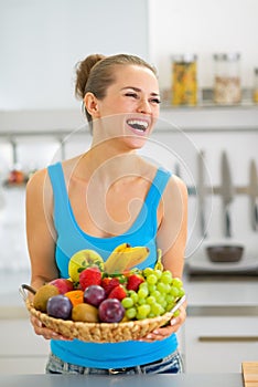 Smiling young woman with fruits plate in kitchen