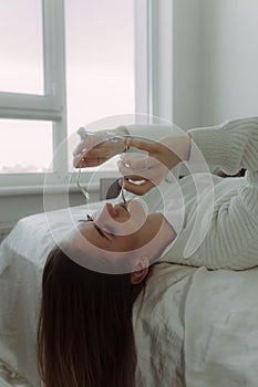 Smiling young woman girl puts on glasses while lying in bed spending time in bedroom at home. Rest mood lifestyle concept