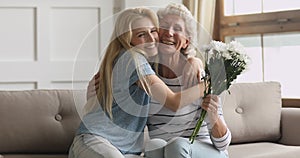 Smiling young woman giving flowers to happy middle aged mother.