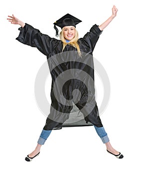 Smiling young woman in graduation gown jumping