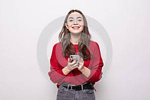 Smiling young woman in gray sweater, scarf using mobile phone typing sms message isolated on grey background