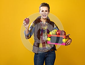 Smiling young woman grower with box of apples showing an apple