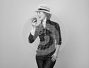 Smiling young woman grower on yellow background eating an apple