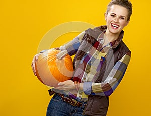 Smiling young woman grower on yellow background holding pumpkin