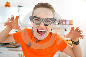 Smiling young woman in Halloween decorated kitchen frightening