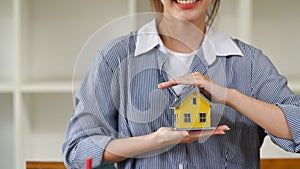 Smiling young woman hand holding house model. New house, insurance and real estate concept.