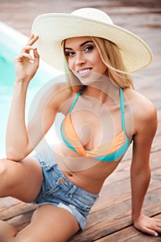 Smiling young woman in hat and shorts near swiming pool