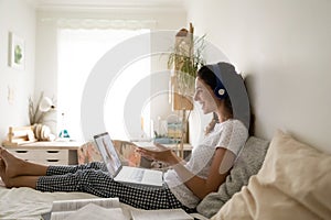 Smiling young woman in headset sit on bed using computer