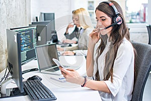 Smiling young woman with headset using phone in office.