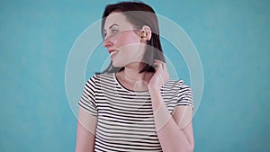 Smiling young woman with hearing impairment hears with hearing aid in ear on blue background