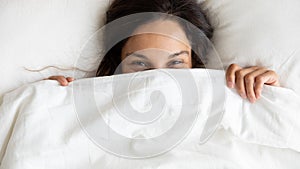 Smiling young woman hide under blanket waking up