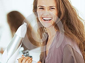 Smiling young woman holding blow dryer