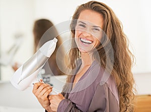 Smiling young woman holding blow dryer