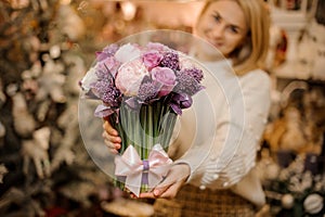 Smiling young woman holding a bouquet of tender pink and purple color flowers with green stalks