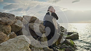 Smiling young woman holding cup of tea and looking on the sunset over cold sea water. Concept of tourism, travel.