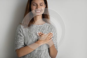 Smiling young woman holding folded hands on chest, feeling thankful.
