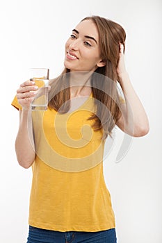 Smiling young woman holding a glass of water on white background. Copy space and mock up. Yellow t shirt. Template blank clothes.