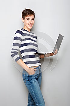 Smiling young woman holding laptop computer against gray background