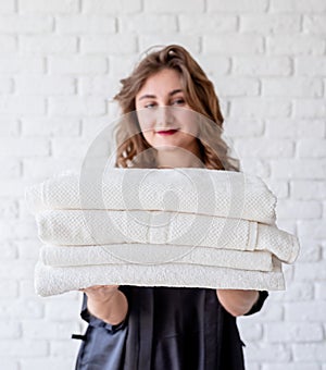 Smiling young woman holding a pile of towels on white bricks background