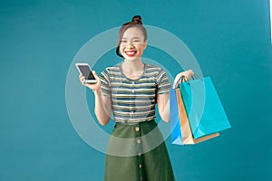 Smiling young woman holding shopping bags, using mobile phone