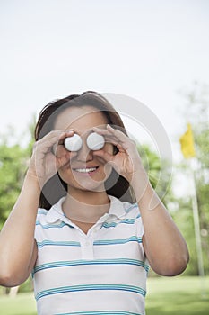 Smiling young woman holding up golf balls in front of her eyes