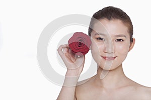 Smiling young woman holding up a red rose next to her ear, studio shot