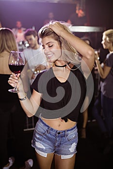 Smiling young woman holding wineglass while dancing at nightclub