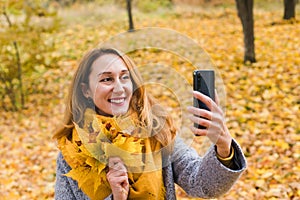Smiling young woman holds autumn yellow leaves takes selfie in the autumn park. Autumn mood. Close-up