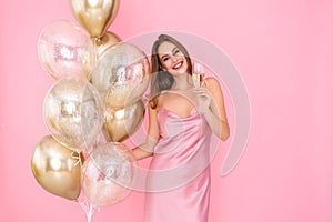 Smiling young woman holds glass of champagne and golden air balloons. came to party. Celebration