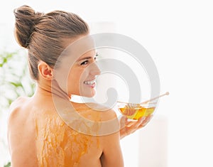 Smiling young woman with honey plate sitting on massage table