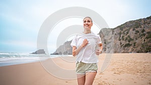 Smiling young woman jogging on sandy beach along sea waves